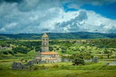 Ancient Romanesque church surrounded by lush countryside under dramatic clouds