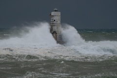Powerful waves crashing against a Mangiabarche lighthouse during a hurricane, symbolizing resilience and the forces of nature