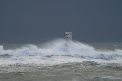 Powerful waves crashing against a Mangiabarche lighthouse during a hurricane, symbolizing resilience and the forces of nature