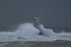 Powerful waves crashing against a Mangiabarche lighthouse during a hurricane, symbolizing resilience and the forces of nature