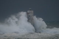 Powerful waves crashing against a Mangiabarche lighthouse during a hurricane, symbolizing resilience and the forces of nature