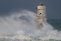 Powerful waves crashing against a Mangiabarche lighthouse during a hurricane, symbolizing resilience and the forces of nature