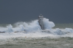 Powerful waves crashing against a Mangiabarche lighthouse during a hurricane, symbolizing resilience and the forces of nature