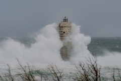 Powerful waves crashing against a Mangiabarche lighthouse during a hurricane, symbolizing resilience and the forces of nature