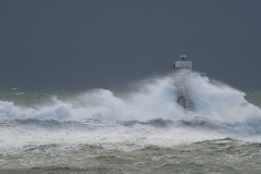 Powerful waves crashing against a Mangiabarche lighthouse during a hurricane, symbolizing resilience and the forces of nature