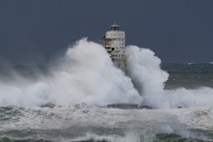 Powerful waves crashing against a Mangiabarche lighthouse during a hurricane, symbolizing resilience and the forces of nature