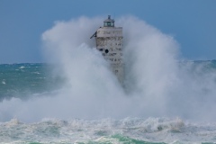 Faro di Mangiabarche avvolto dagli spruzzi del mare in burrasca